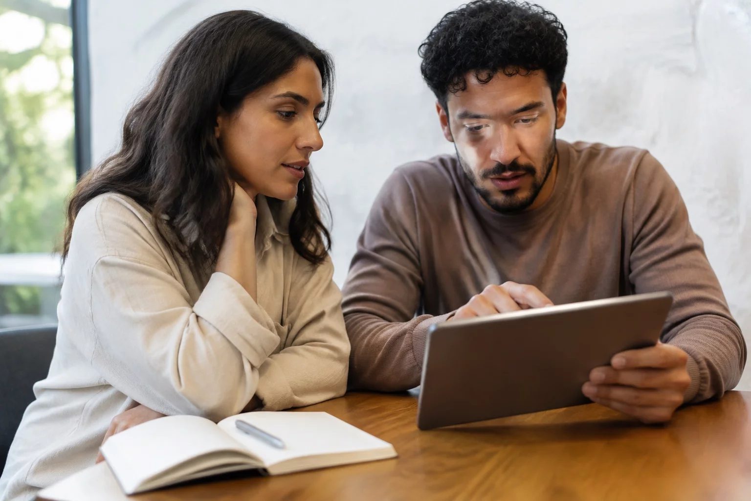 Duas pessoas revisando anotações em um tablet sobre uma mesa de madeira